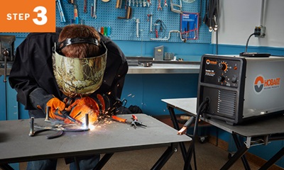 Welder welding metal with Hobart Handler 125 to his right